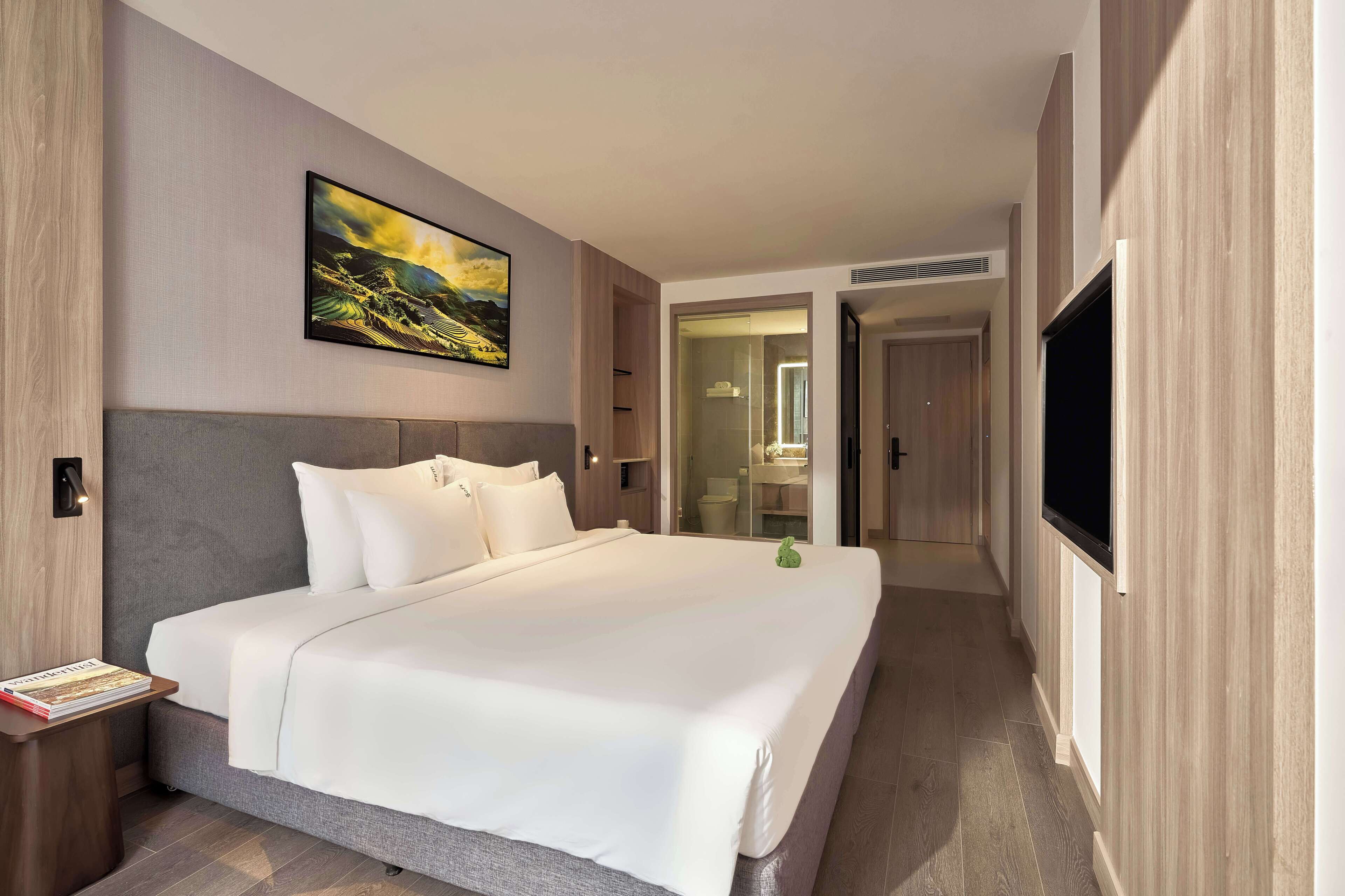 A modern hotel room with a large bed, a flat-screen TV, and a painting on the wall.