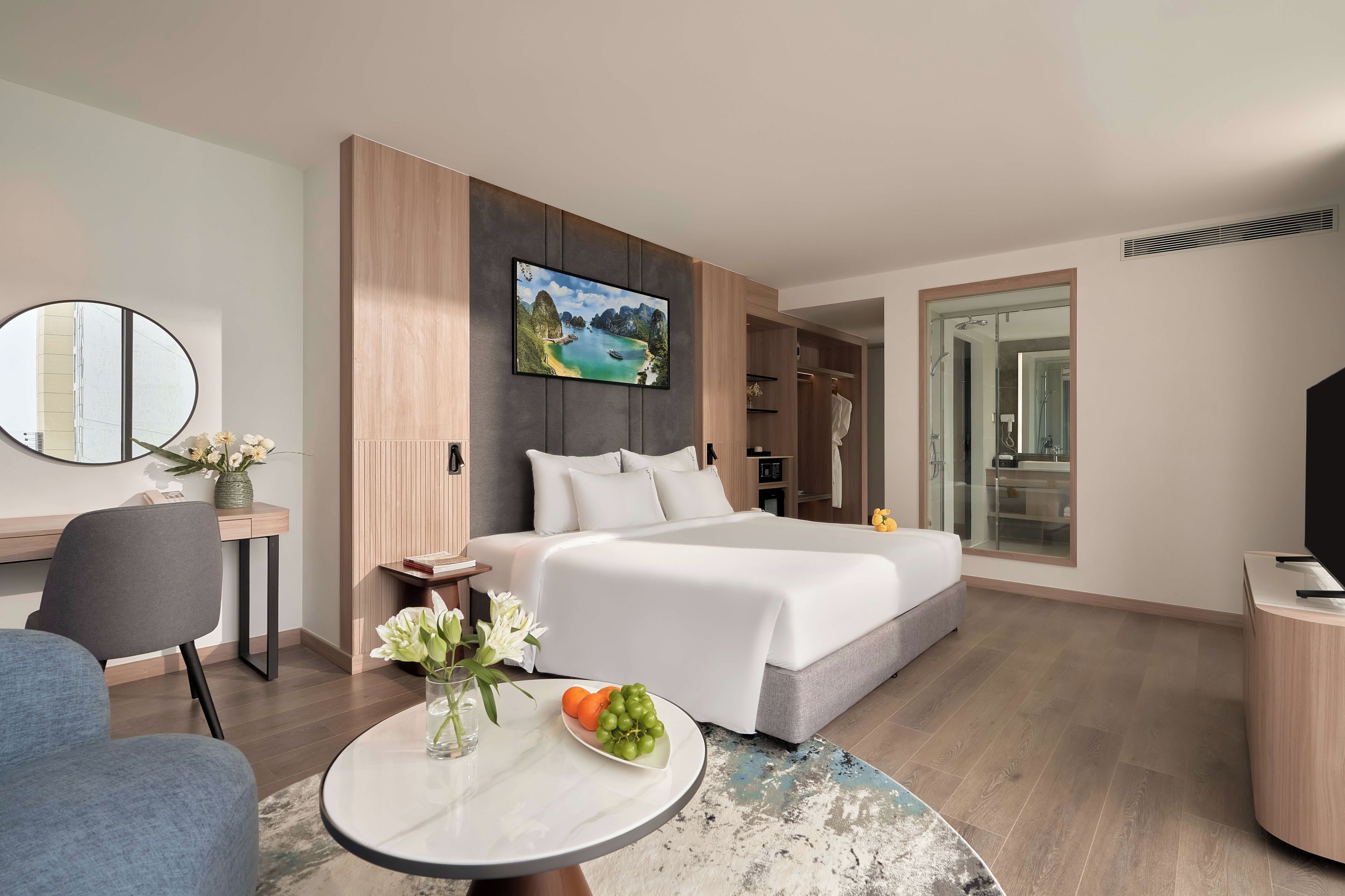 Une chambre d’hôtel moderne avec un lit, un bureau, une table ronde agrémentée de fleurs et un tableau au mur.