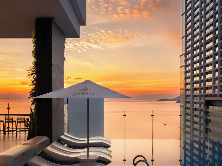 A modern hotel with a view of the sunset over the water, lounge chairs, and a unique architectural design.