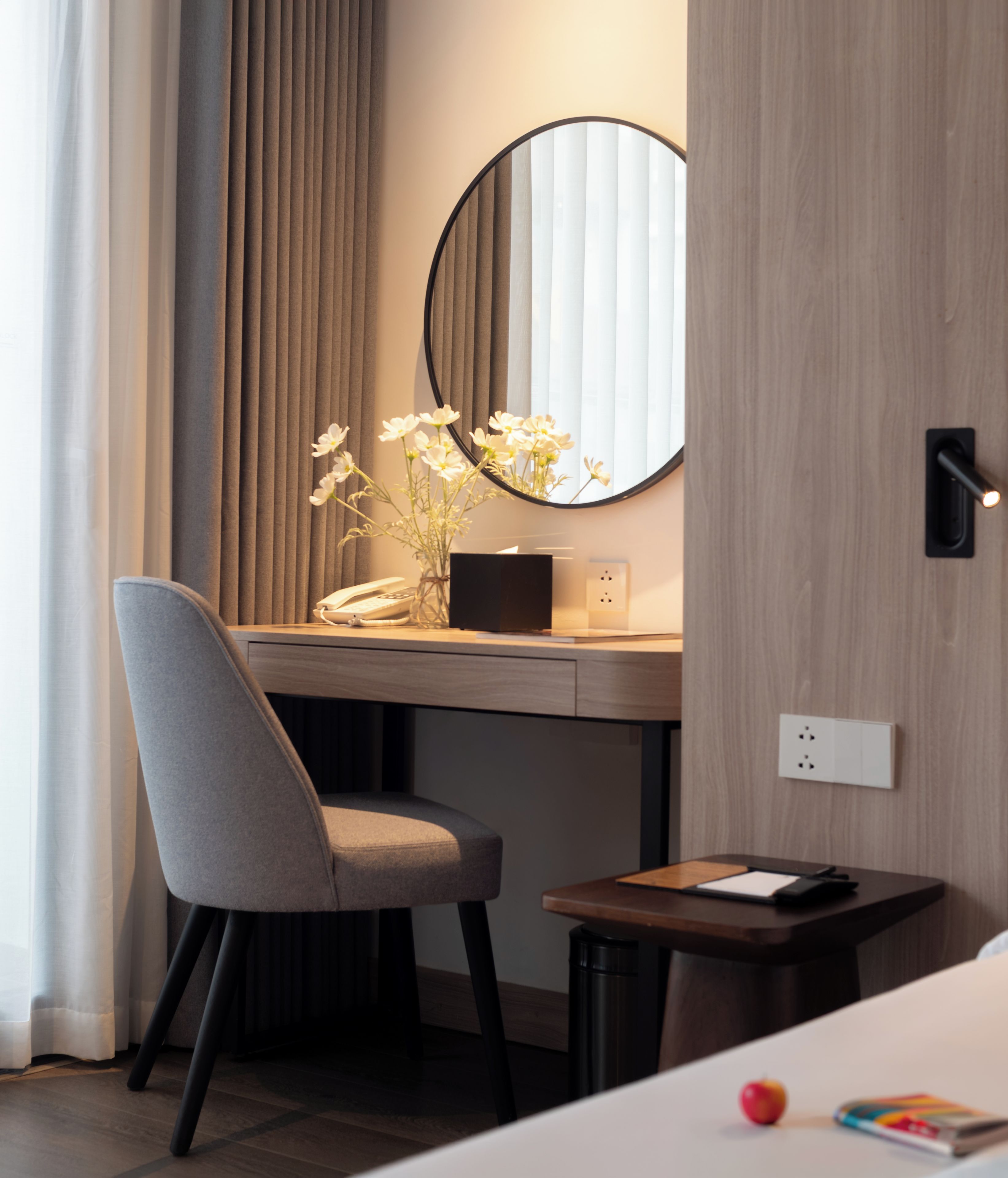 Ein modernes Hotelzimmer mit Schreibtisch, Stuhl, Nachttisch und einer kleinen Nachttischlampe.