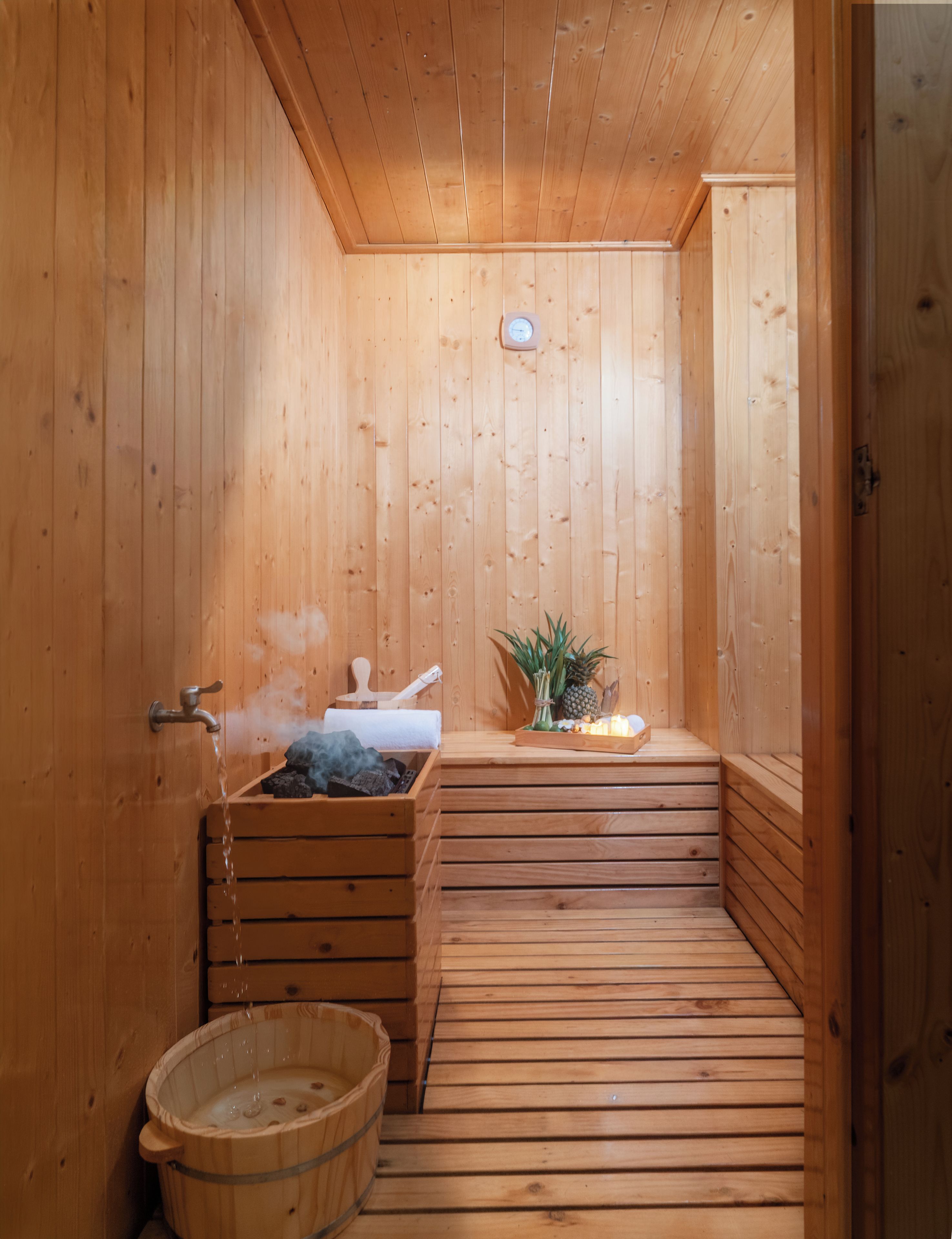 A wooden sauna with a bench, a small table with a pineapple, and a bucket.