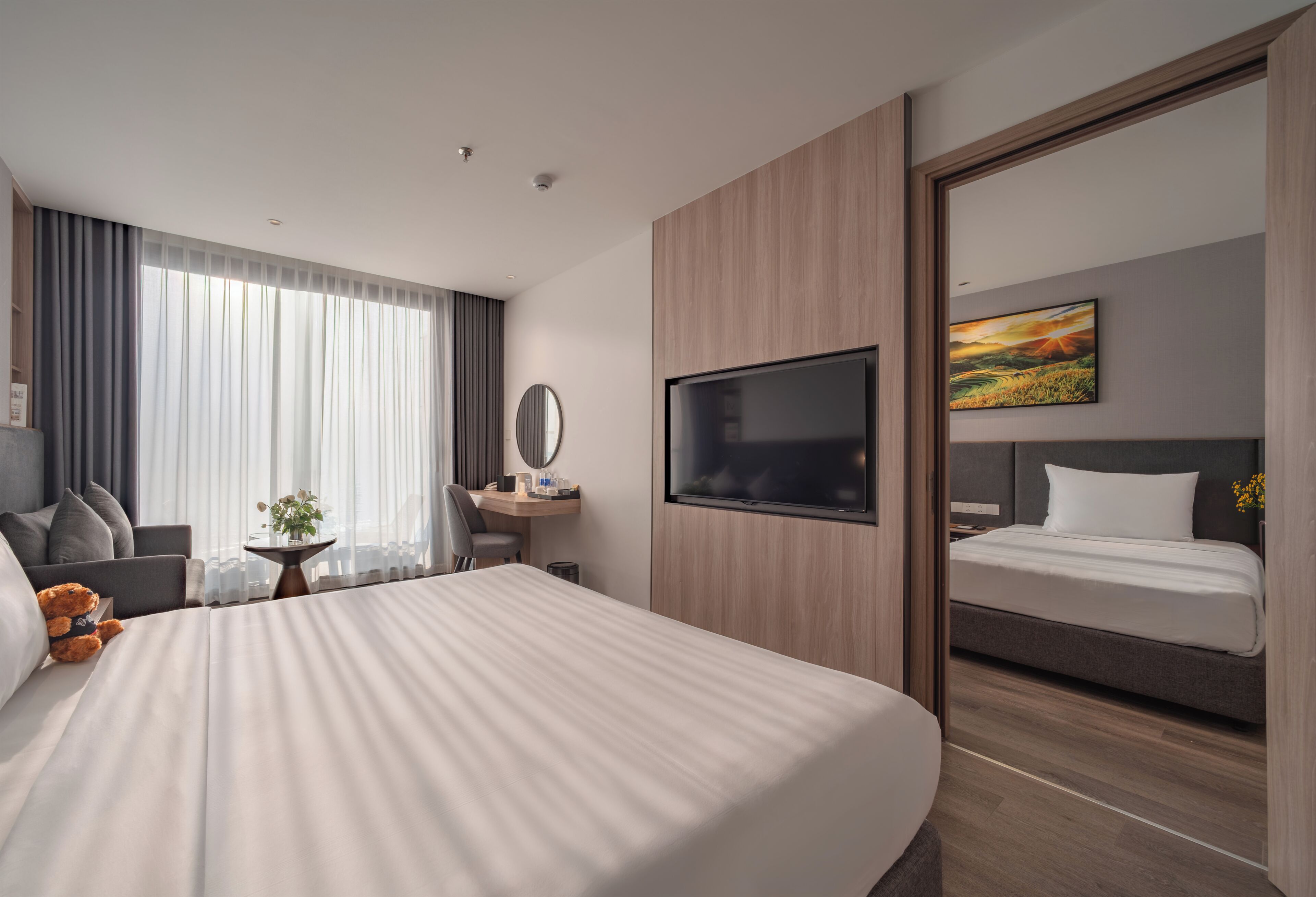 A modern hotel room with a large bed, a desk with a chair, a television, and a painting on the wall.
