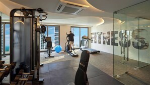 Un gimnasio moderno con equipo de ejercicio, ventanas amplias y un muro de cristal con carteles motivacionales.