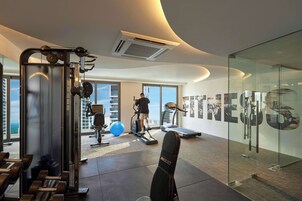 Une salle de sport moderne équipée de matériel d’exercice, dotée de grandes fenêtres et d’un mur en verre orné d’affiches motivantes.