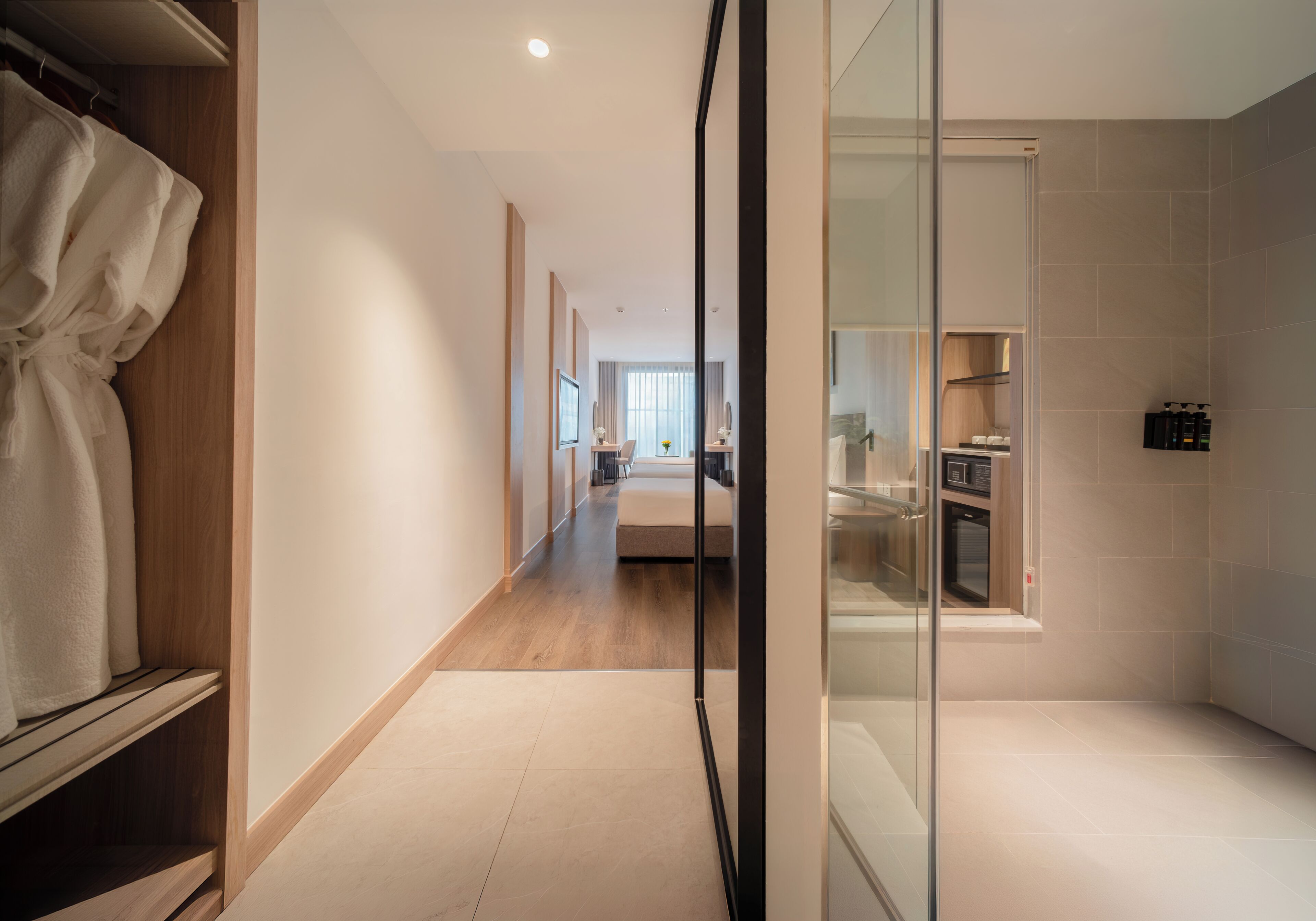 A hotel room with a wooden floor, a glass shower enclosure, a bed, and a small kitchenette.