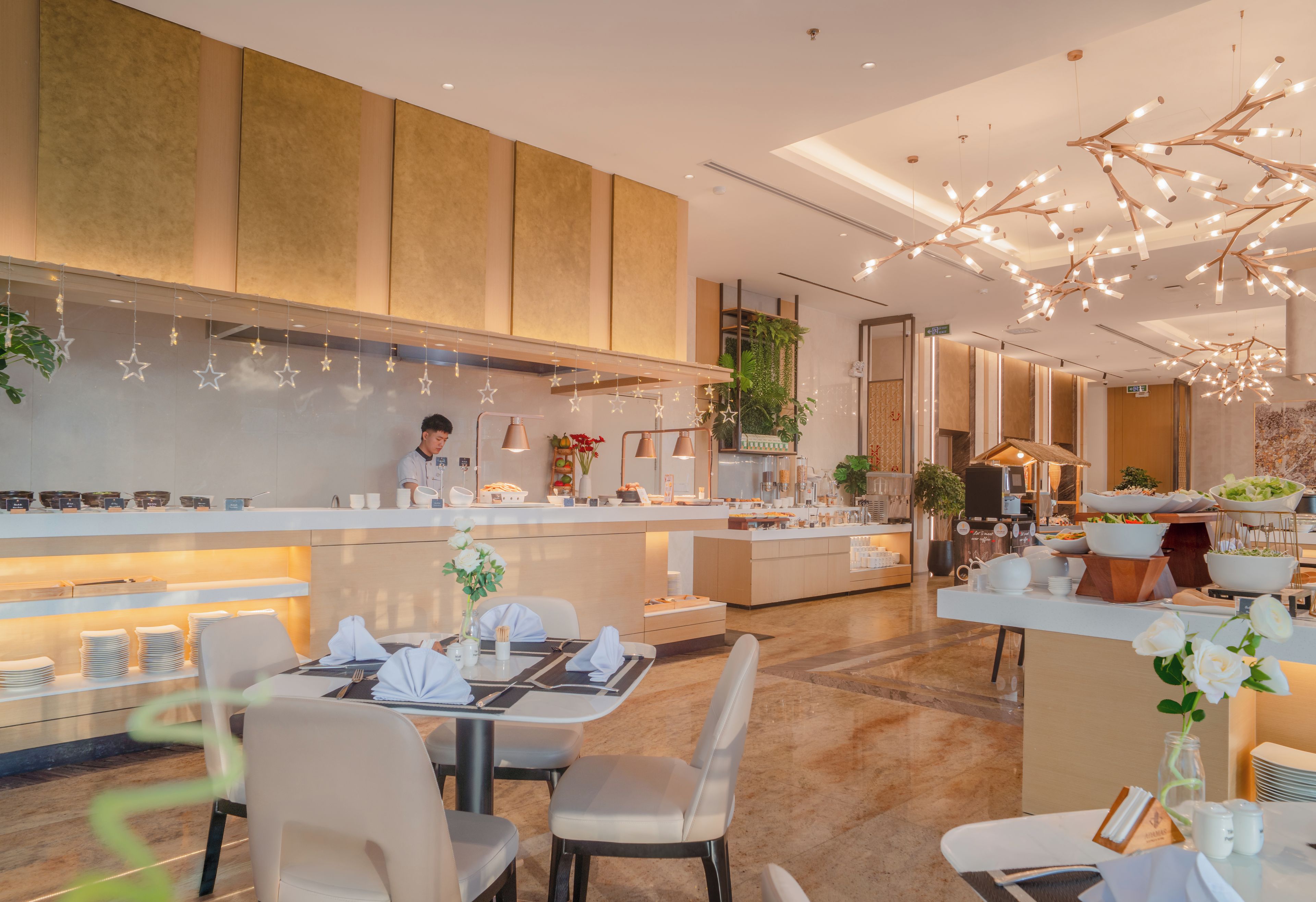 A modern hotel restaurant with a central counter, seating area, and a bar.