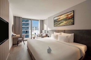 A hotel room with a large bed, a desk with a chair, a TV, and a painting on the wall.