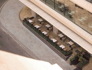An outdoor seating area with tables and chairs, surrounded by greenery, and adjacent to a building with a glass facade. - Adamas Boutique Hotel Nha Trang (Nha Trang)