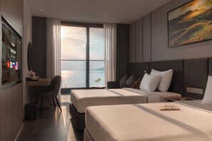 Habitación de hotel con dos camas, un escritorio, una silla, televisión y un ventanal con vista al agua.
