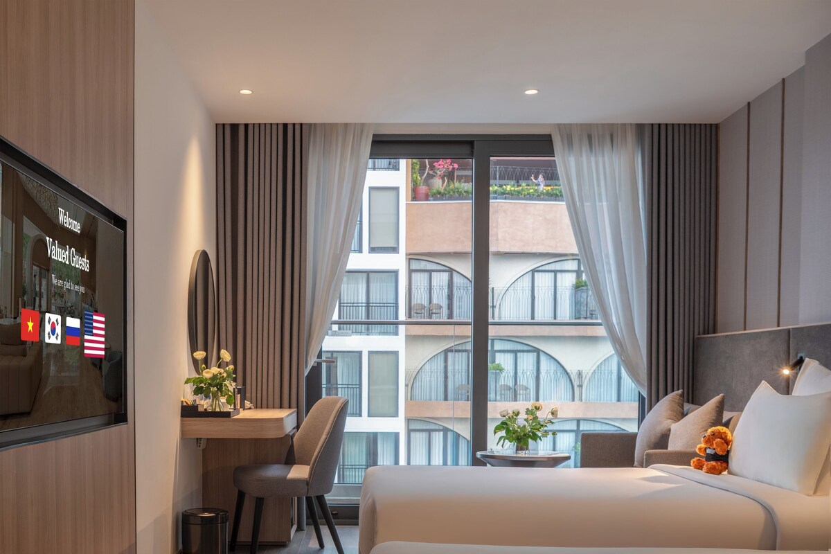 Habitación de hotel con cama, escritorio, silla, televisión y vista del edificio.