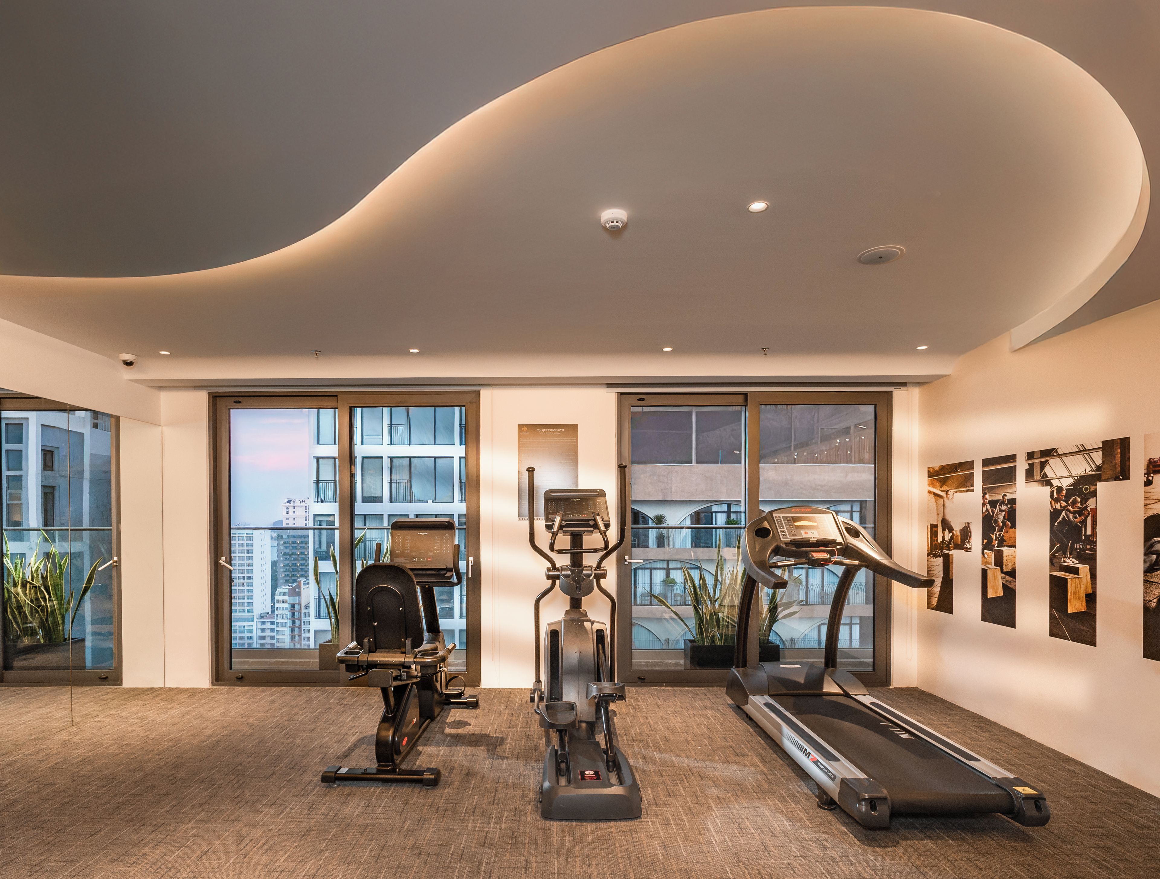 Une salle de sport moderne équipée de machines de cardio, dotée de grandes fenêtres et offrant une vue sur le paysage urbain.