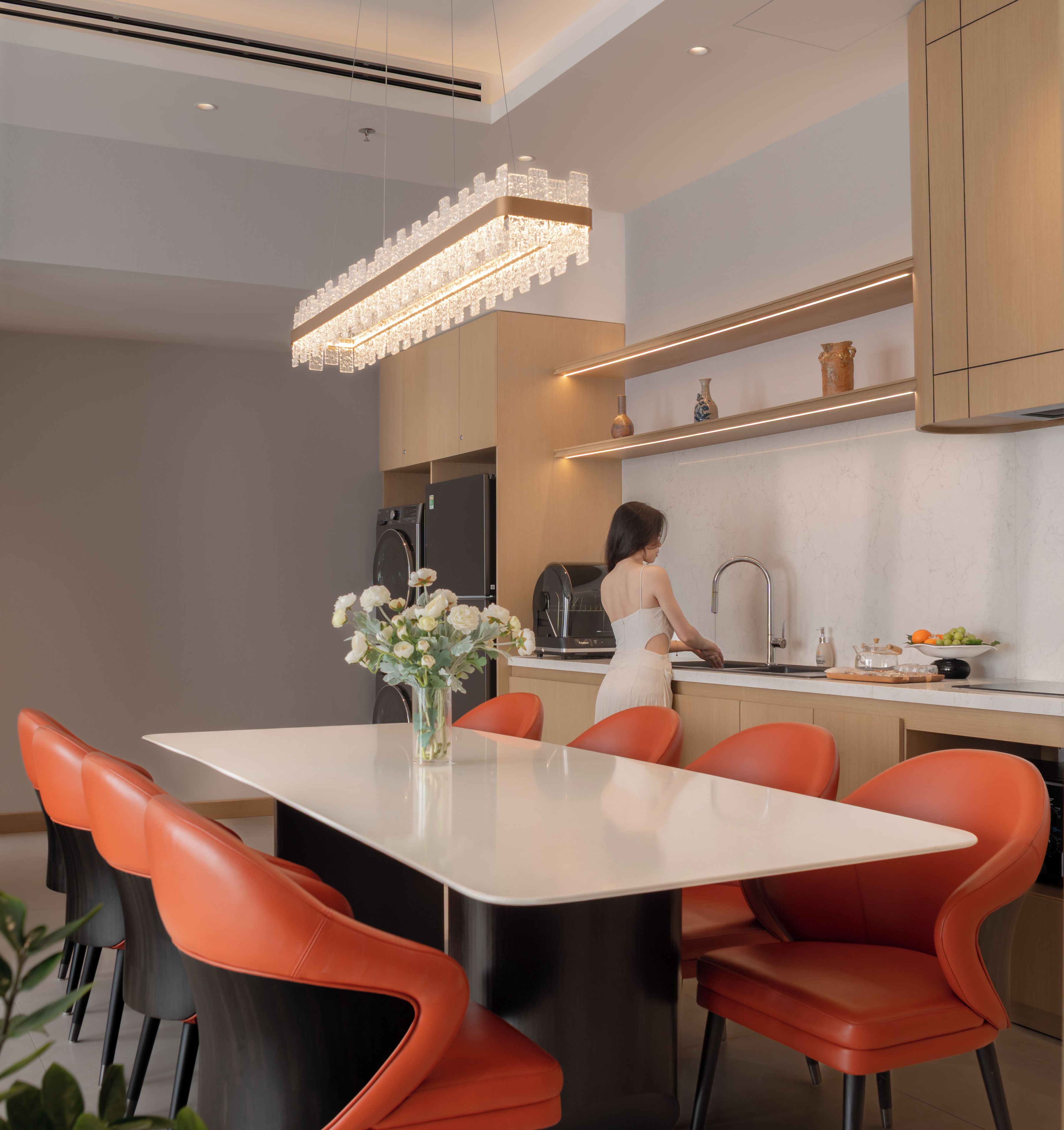 A modern kitchen with a central island, red chairs, and a woman washing dishes.