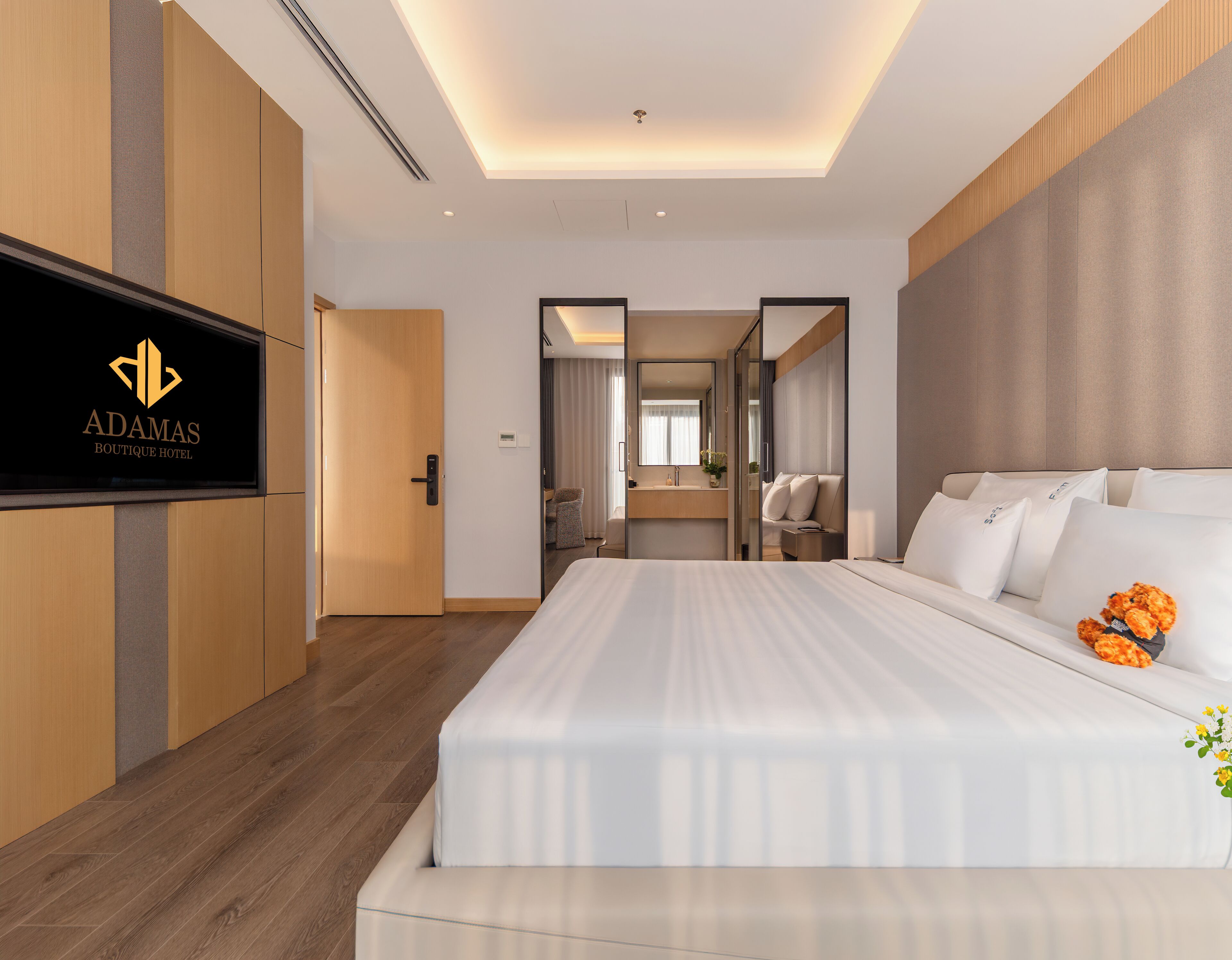 A hotel room with a bed, a television, a bathroom, and a view of the hallway.