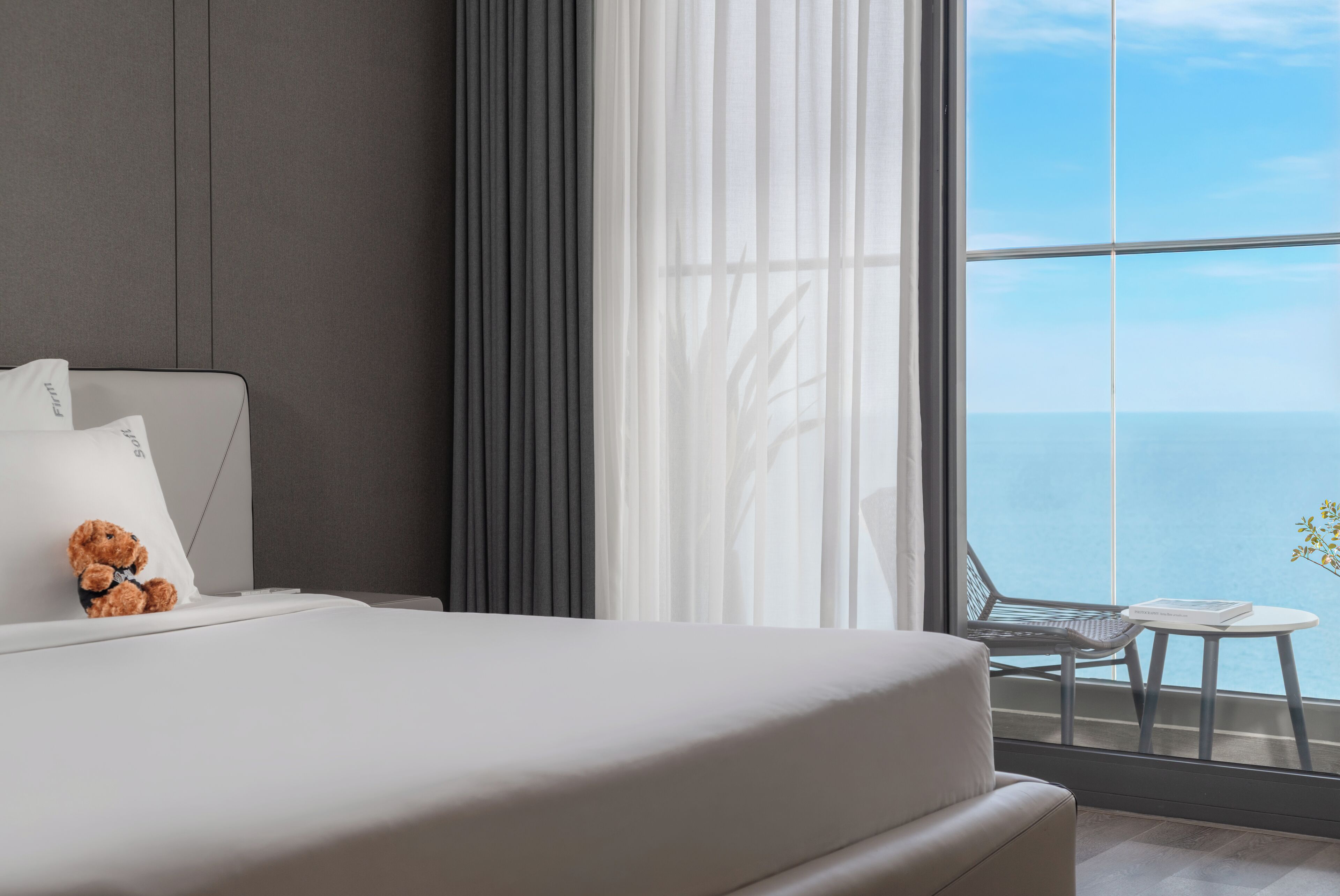 A modern bedroom with a large window, a bed, a small table, and a teddy bear.