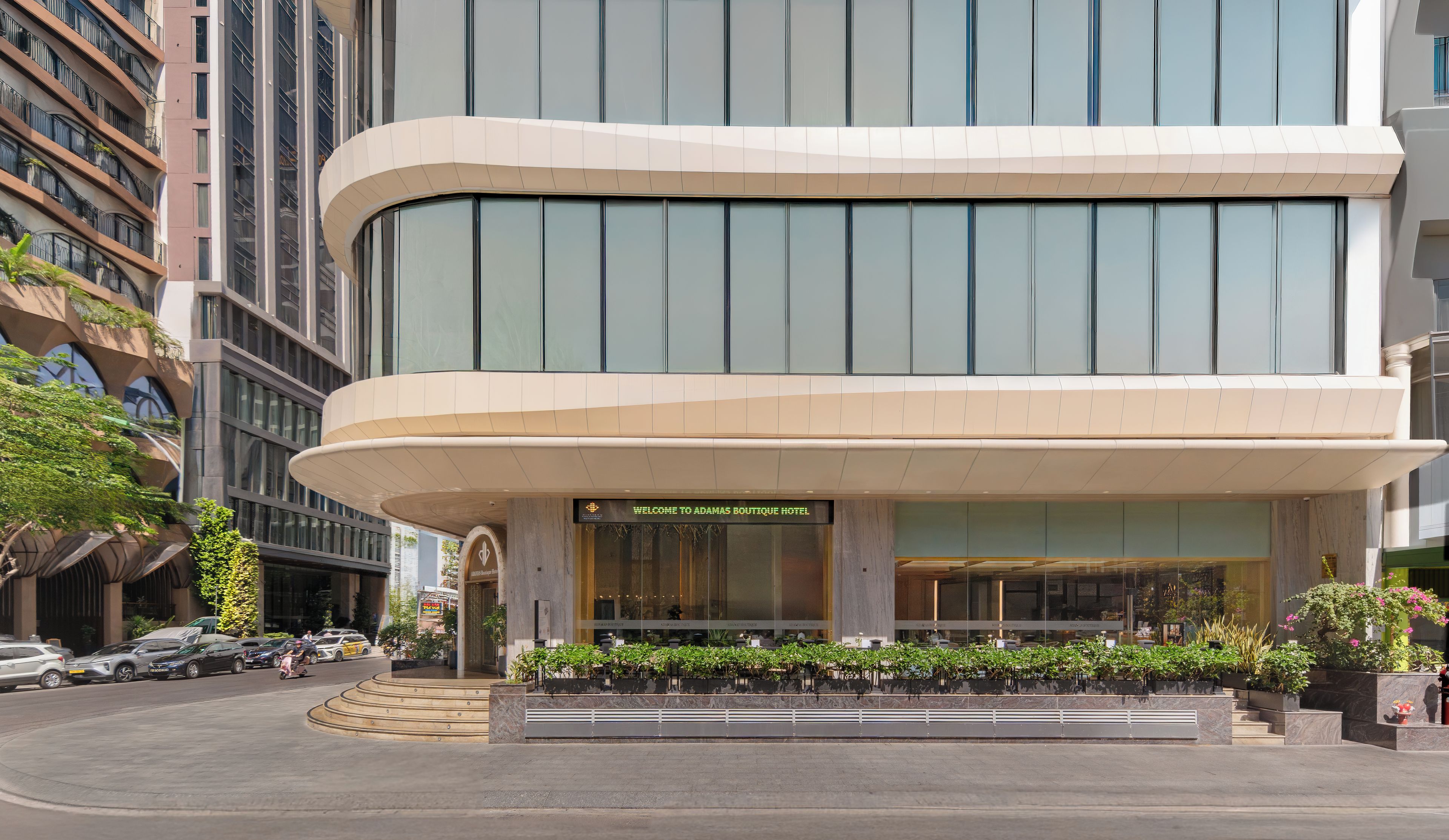 Une entrée d’hôtel moderne, avec une façade incurvée, de grandes fenêtres et une enseigne accueillante.