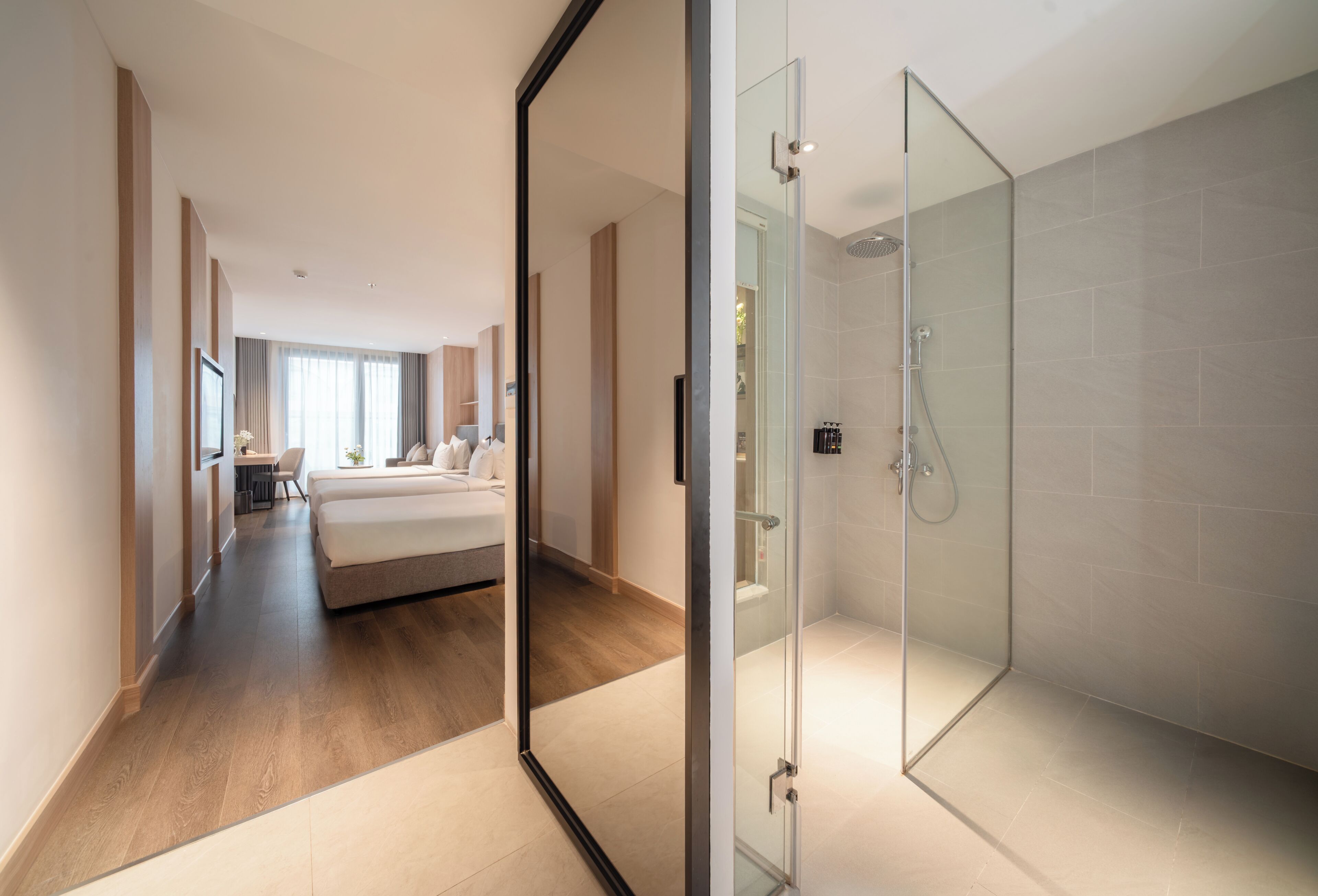 Een moderne hotelkamer met een douchecabine van glas, een bed en uitzicht op de gang.