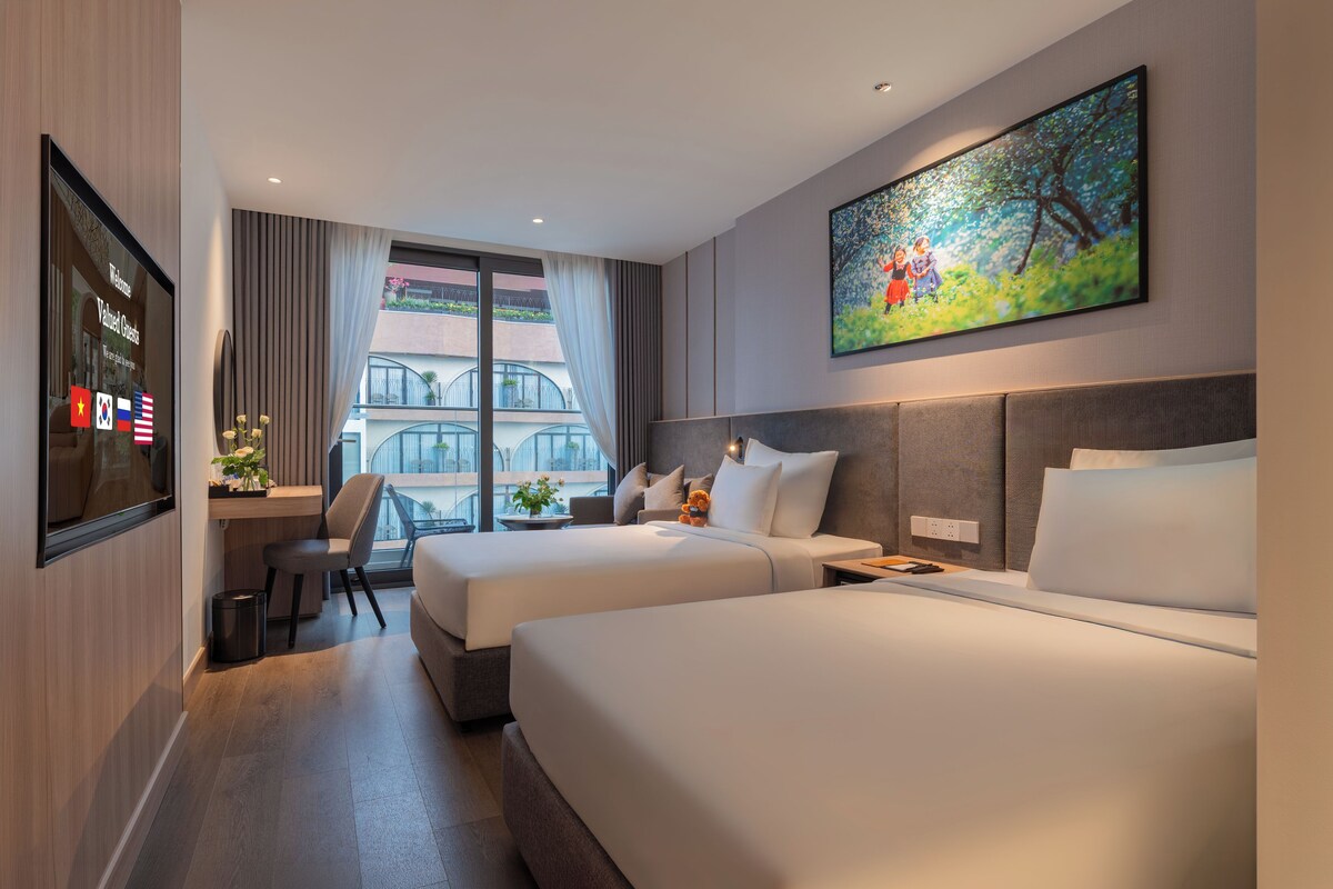 A hotel room with two beds, a desk, a chair, a TV, and a balcony with curtains.