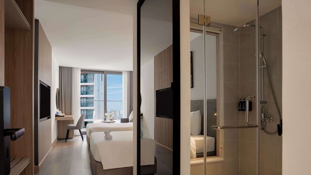 Una habitación de hotel moderna con cama, escritorio, silla y zona de ducha.
