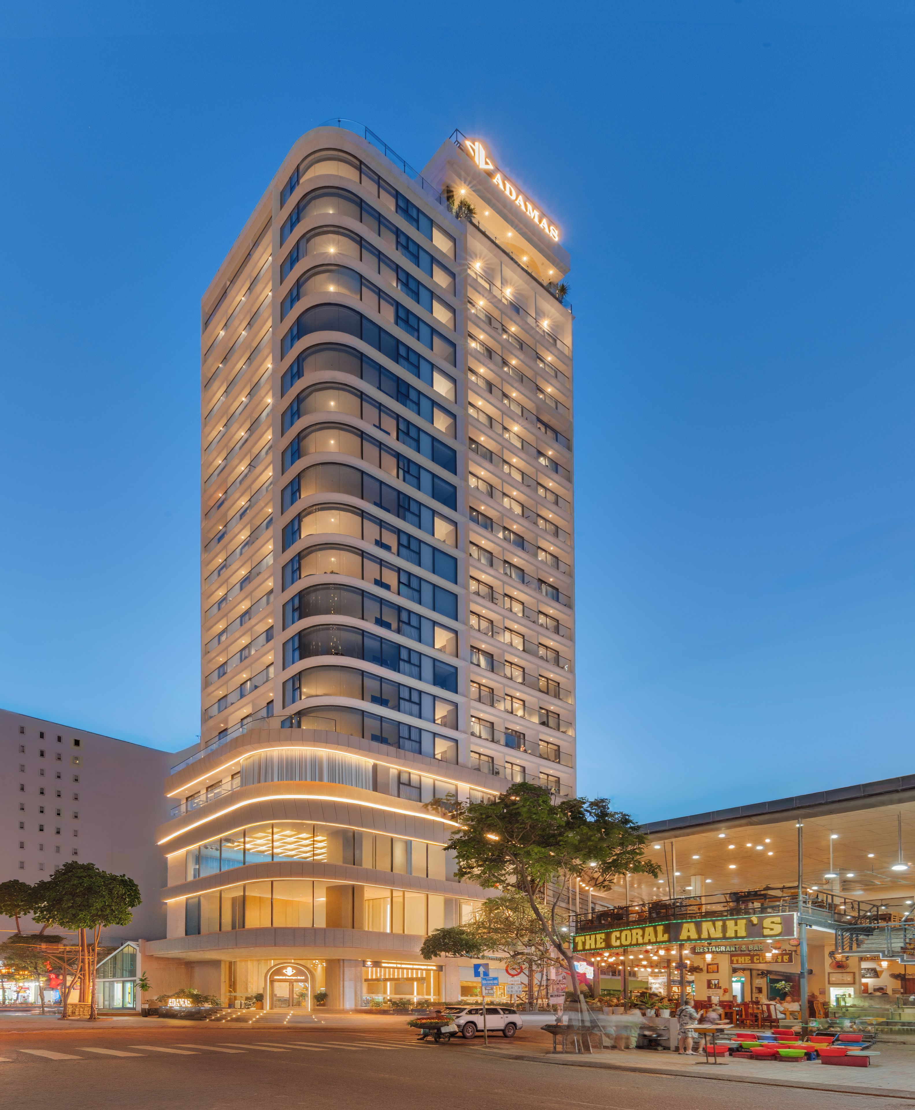 A high-rise hotel with a curved facade, multiple balconies, and a well-lit entrance.
