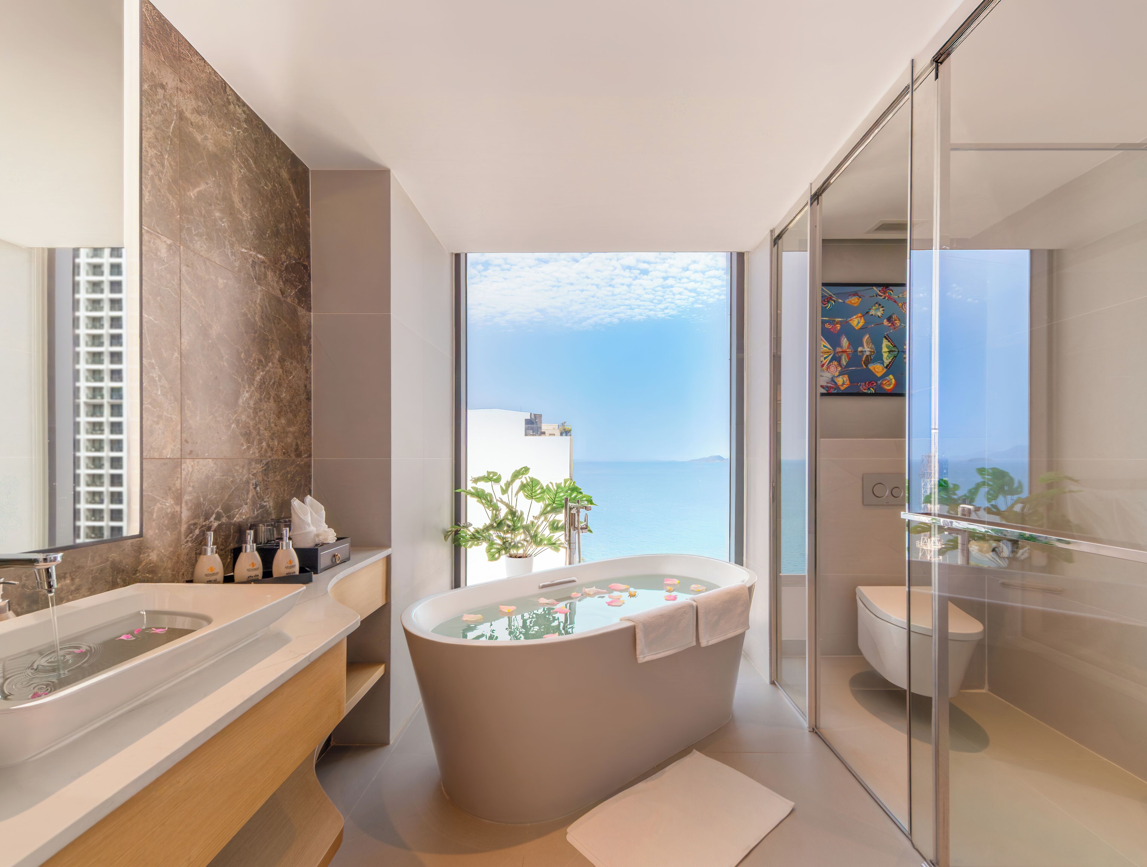 A modern bathroom with a bathtub, a large mirror, and a view of the sea.
