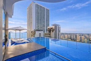 A rooftop infinity pool with a view of a city skyline and a mountain in the distance.