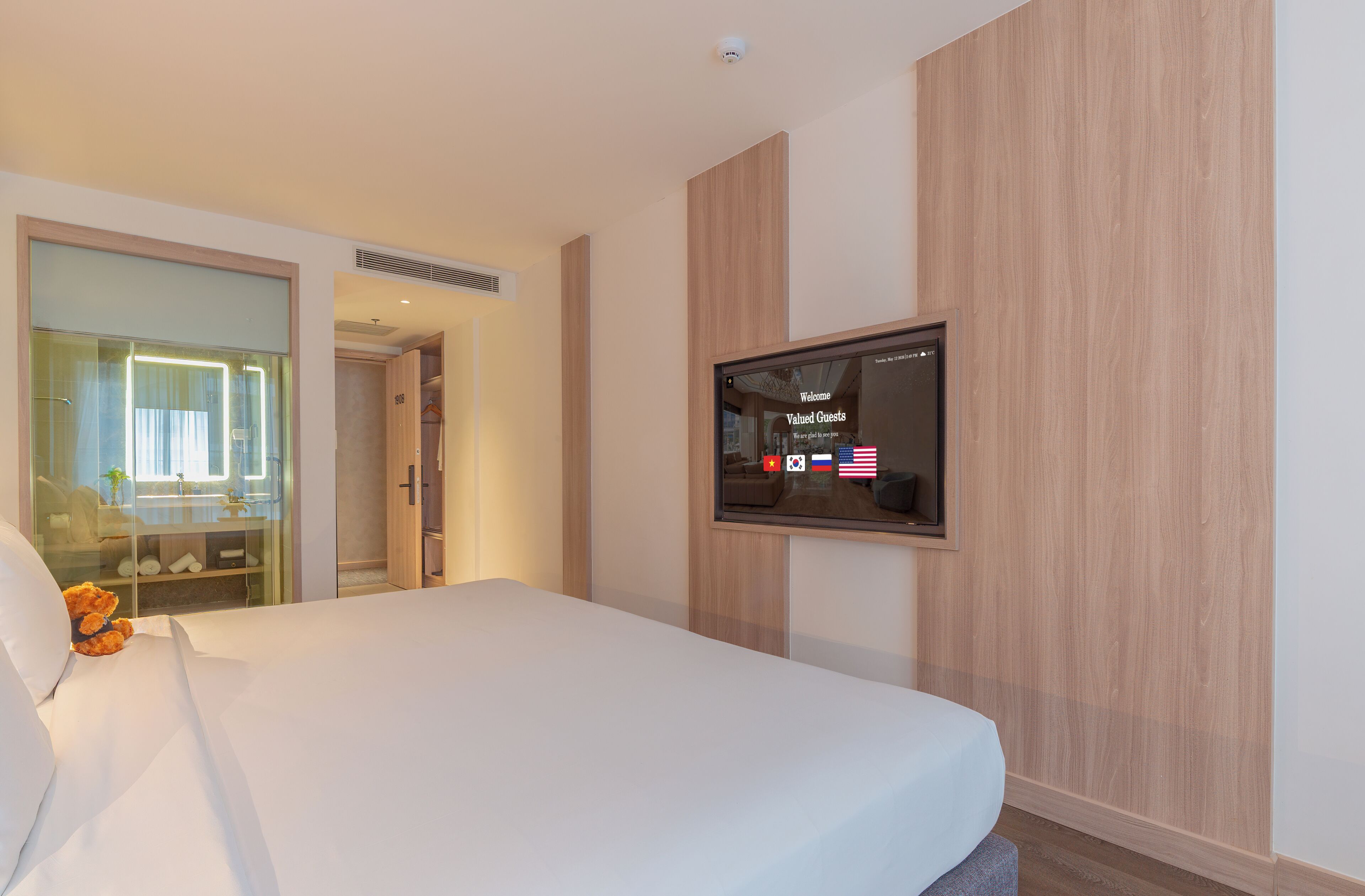 Habitación de hotel con cama, televisor montado en la pared, baño con cabina de ducha de vidrio y pared revestida de paneles de madera.