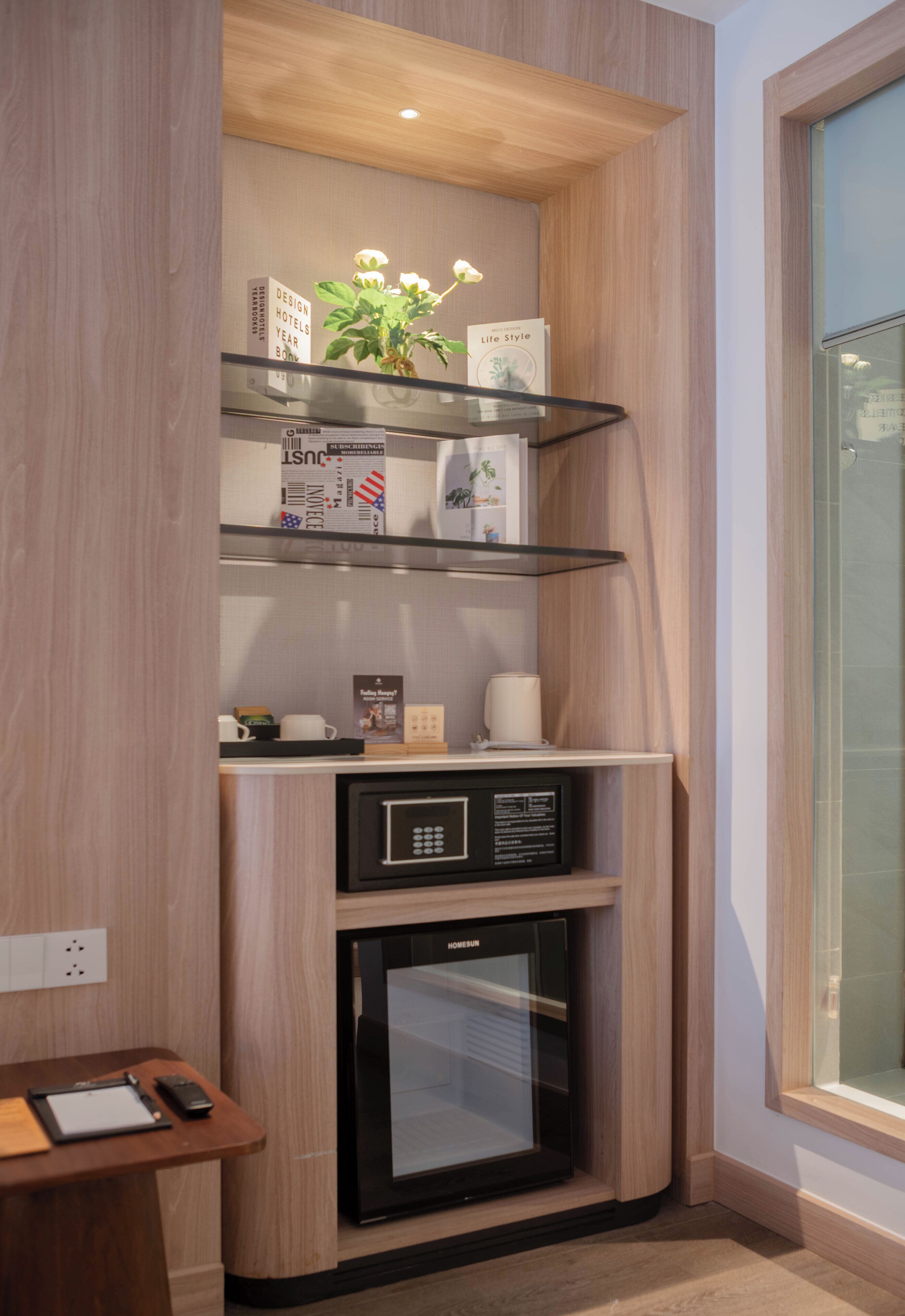 A compact minibar with a coffee machine, a small refrigerator, and a glass shelf with a plant and a book.