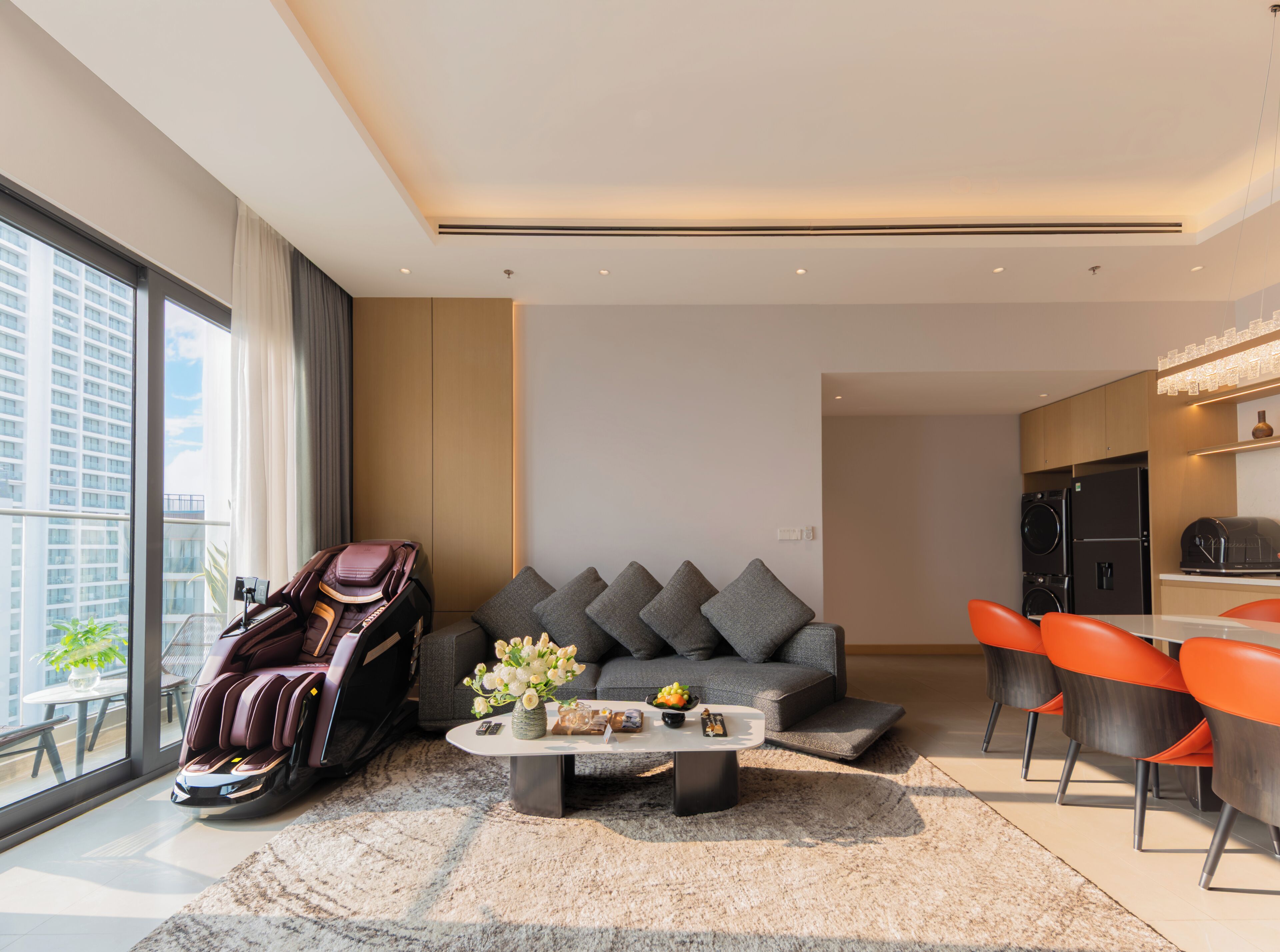 A modern living room with a massage chair, grey sofa, and orange chairs.