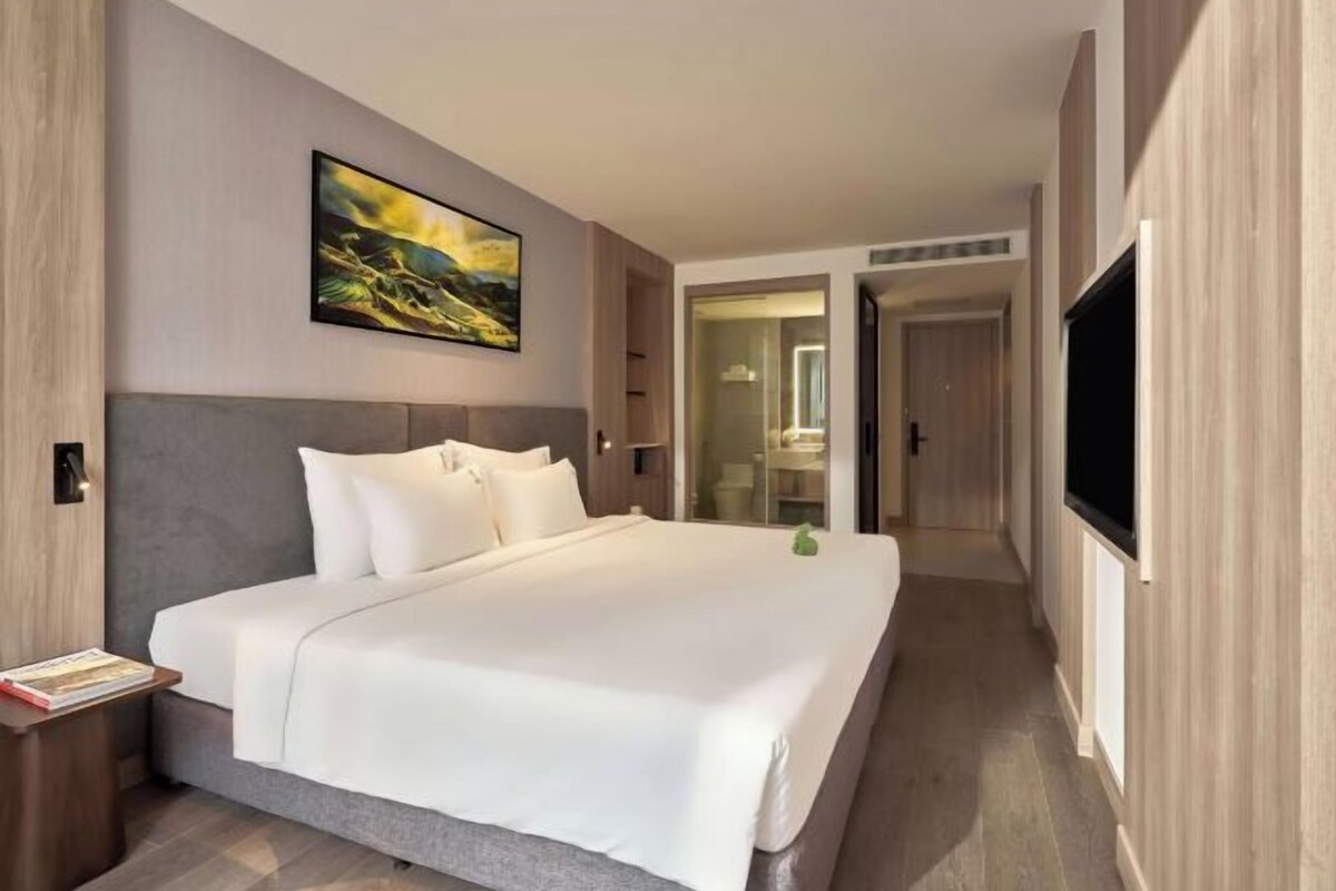 A modern hotel room with a large bed, a flat-screen TV, and a painting on the wall.