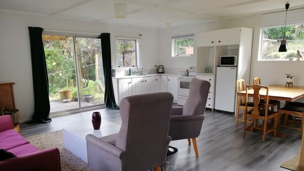 A modern living room with a sofa, a dining table with chairs, and a kitchen area with cabinets and appliances. - 2 bedroom holiday home with outdoor bath & sauna (Upper Hutt)