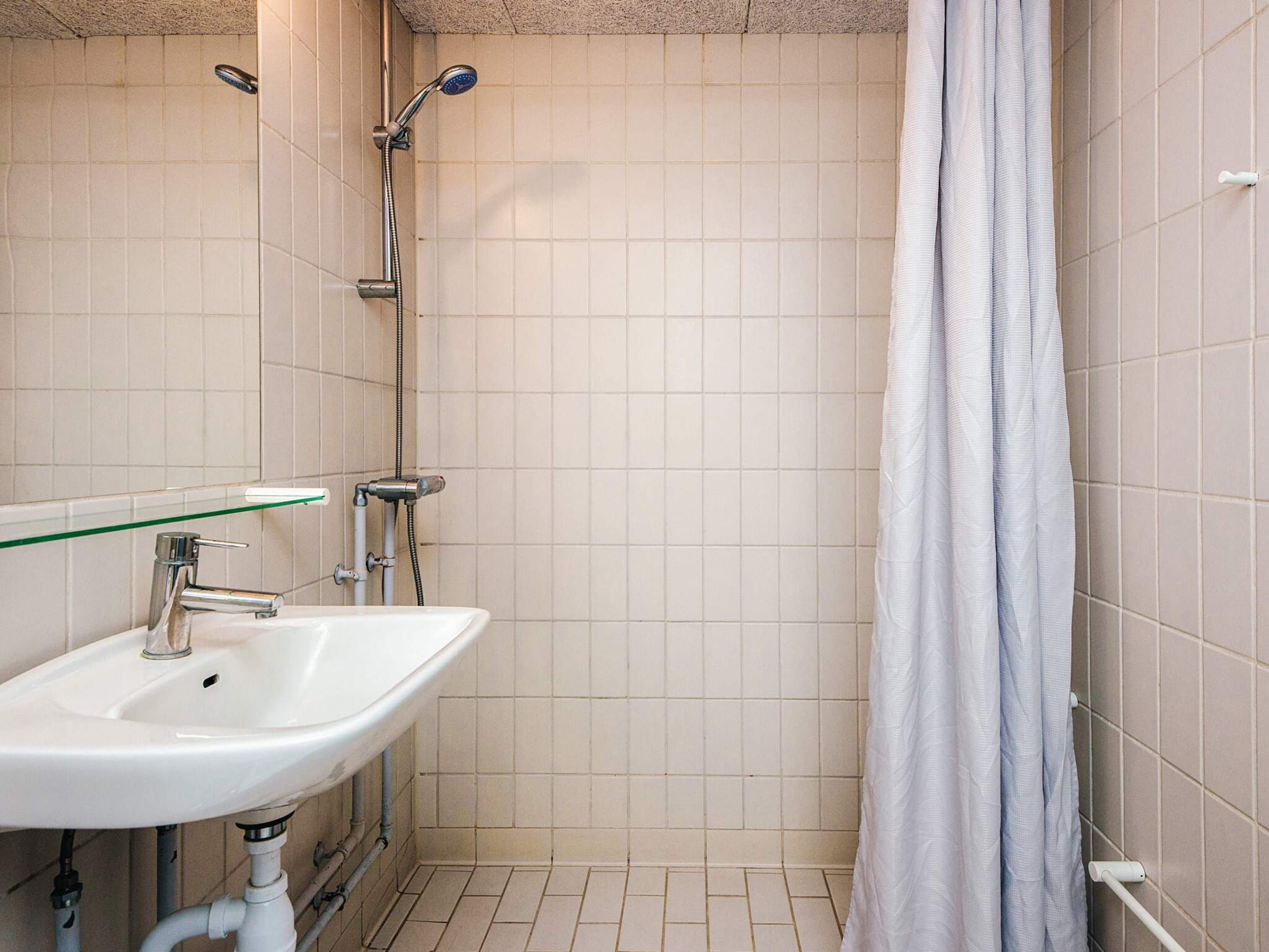 A bathroom with a white sink, a glass shelf, a shower with a handheld showerhead, and a white shower curtain.