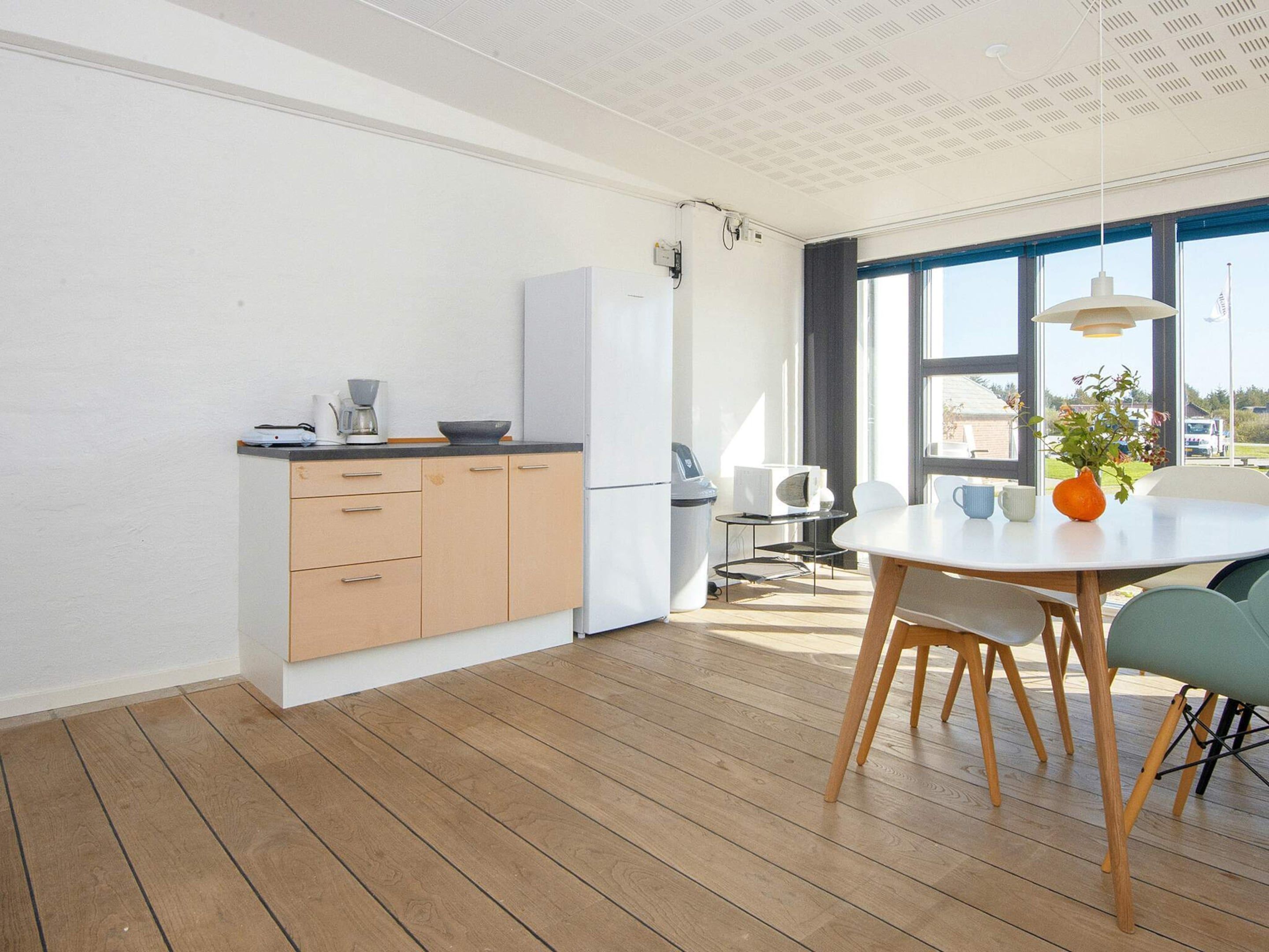 A modern kitchen with wooden cabinets, a white refrigerator, and a dining area with a round table and chairs.
