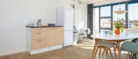 A modern kitchen with wooden cabinets, a white refrigerator, and a dining area with a round table and chairs.