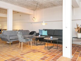 Una sala moderna con un sofá gris, un sillón a juego, dos mesitas redondas y una lámpara colgante.