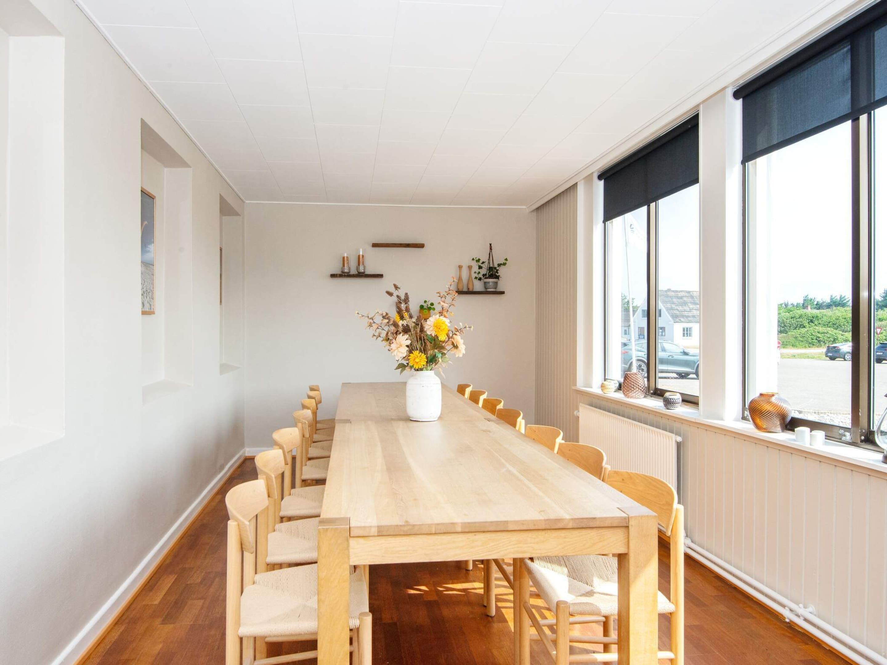 A long dining table with chairs, a vase of flowers, and a view of the outside through large windows.