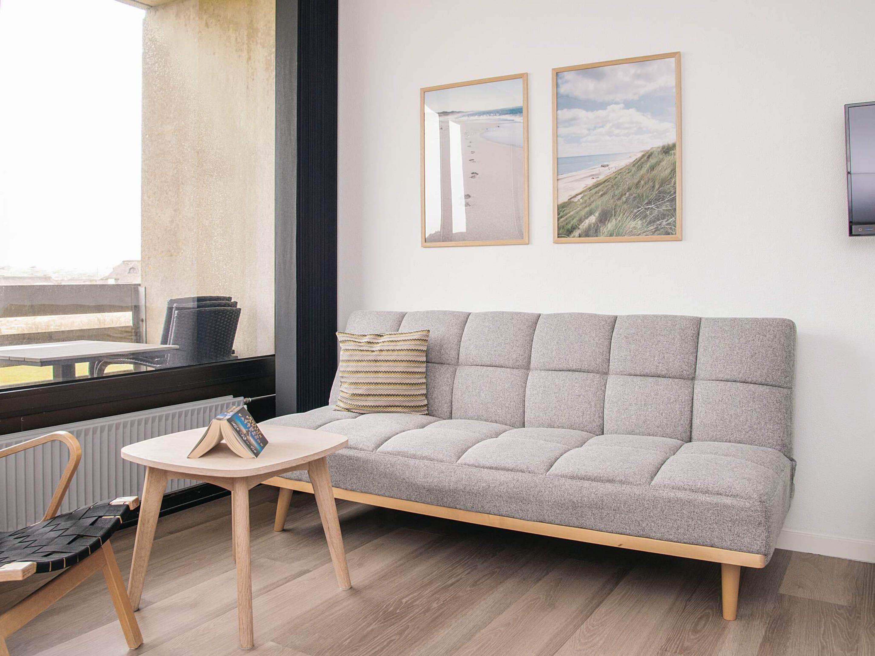 A modern living room with a grey sofa, a small round table, and two framed pictures on the wall.