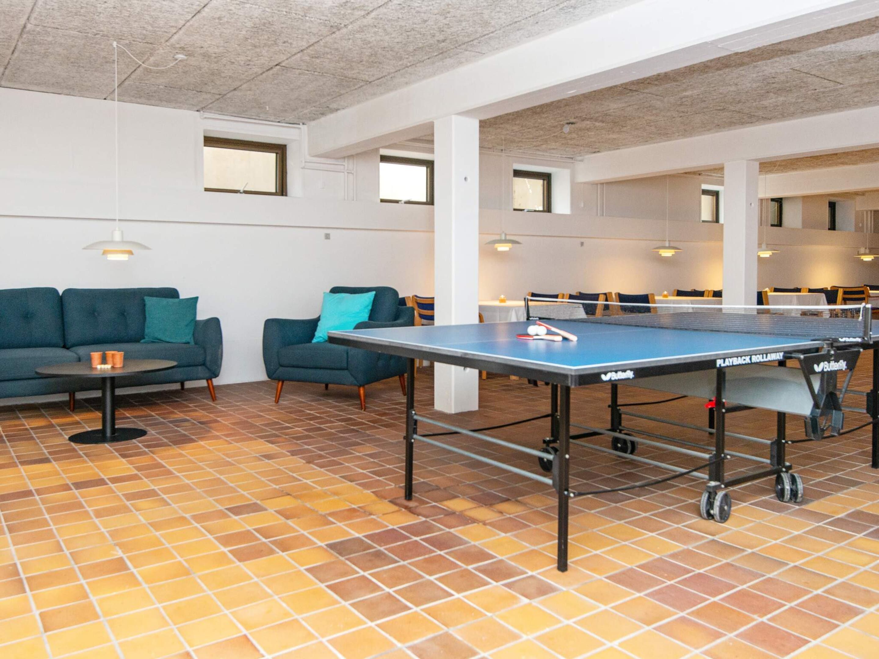 A ping pong table in a communal area with a tiled floor, sofas, and tables.