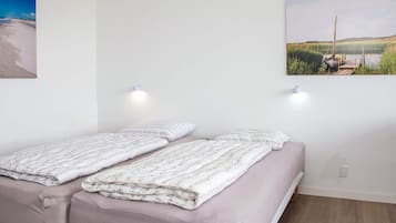 A double bed with a floral duvet, a single bed with a plain duvet, two wall-mounted lights, and a landscape painting on the wall.