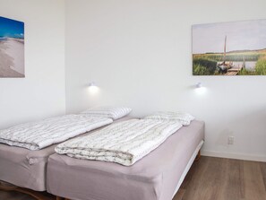 A double bed with a floral duvet, a single bed with a plain duvet, two wall-mounted lights, and a landscape painting on the wall. - 3 Person Holiday Park Home in Ulfborg (Ulfborg)