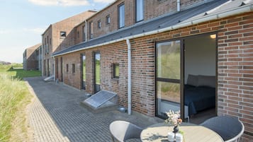 A modern brick building with large windows and a patio area featuring wicker furniture and a table.