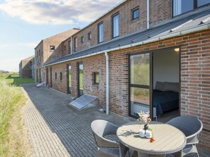 A modern brick building with large windows and a patio area featuring wicker furniture and a table. - 3 Person Holiday Park Home in Ulfborg (Ulfborg)