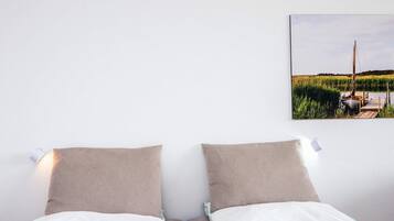 Una cama con dos almohadas, una colcha blanca y un cuadro colgado en la pared de un barco en un lago.