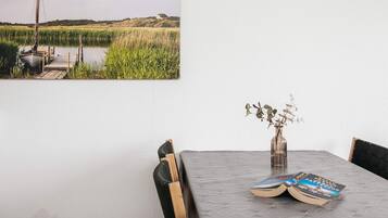 A dining table with a vase of dried flowers and books, a chair, and a wall-mounted painting of a landscape.
