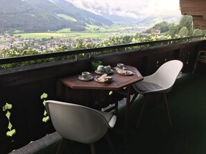 Un balcon avec une table préparée pour le thé, donnant sur une vallée parsemée de maisons et bordée de montagnes.