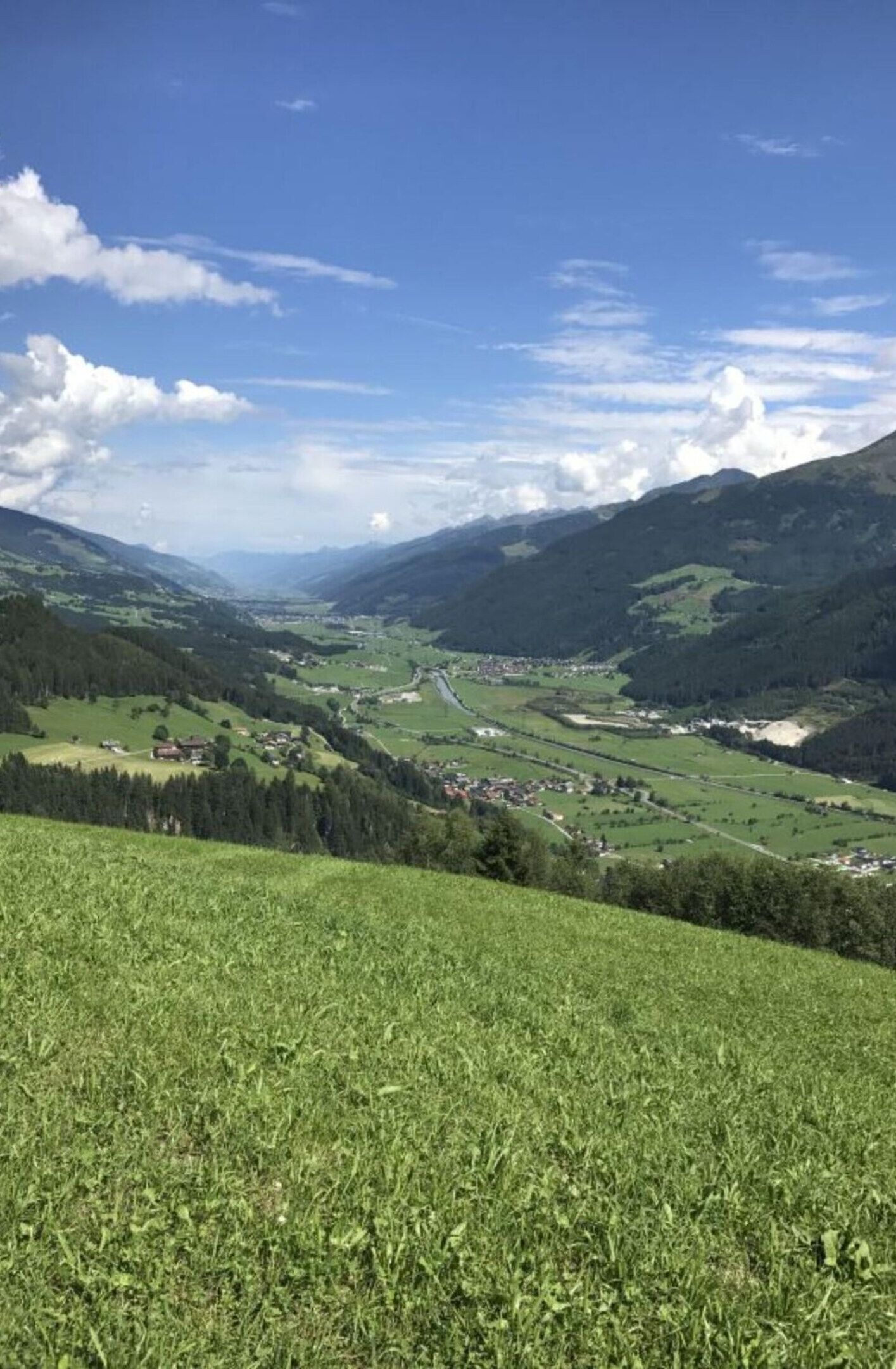 Ein weites Panorama eines Tals mit einer kleinen Stadt, eingebettet zwischen grünen Hügeln und Bergen.