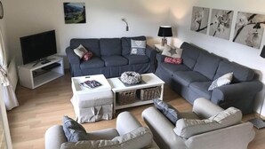 Un salon avec deux canapés gris, une table basse blanche, un téléviseur posé sur un meuble et une cheminée.
