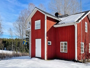 A red wooden house with a white door and windows, surrounded by snow and trees. - 6 Person Holiday Home in Tocksfors (Töcksfors)