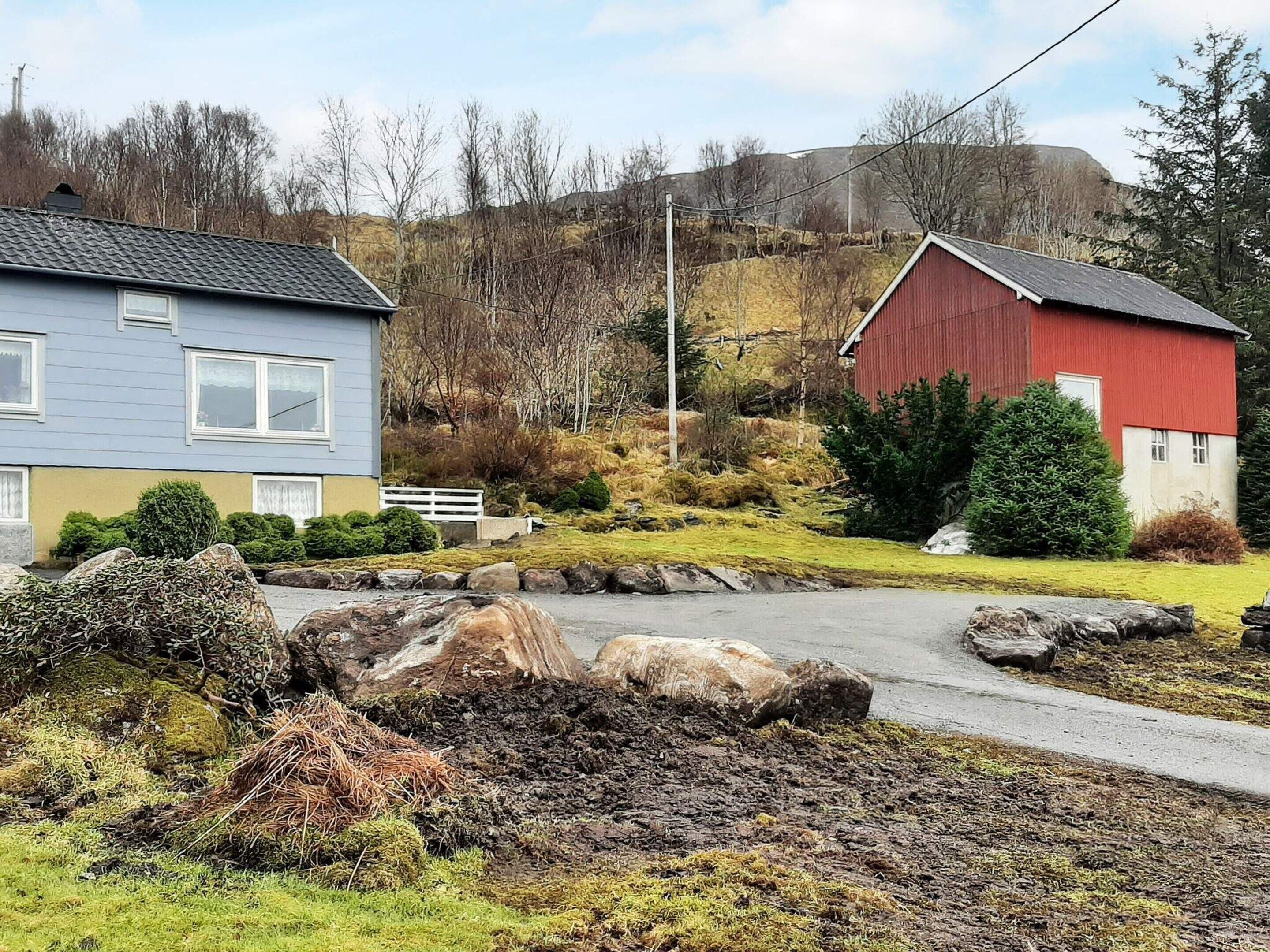A rural setting with a blue house, a red barn, and a stone wall.