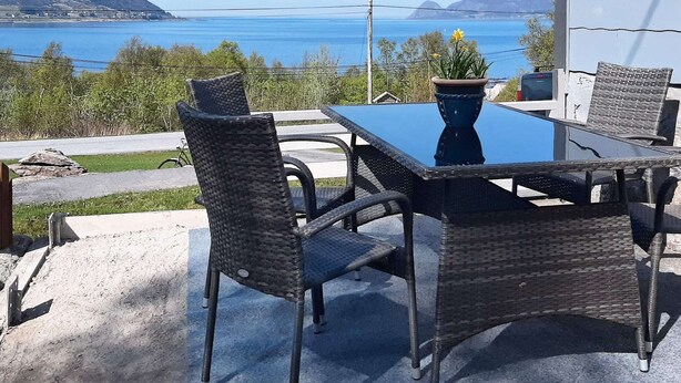 An outdoor dining area with wicker chairs and a table, overlooking a body of water and hills. - 6 Person Holiday Home in Aram (Vanylven)