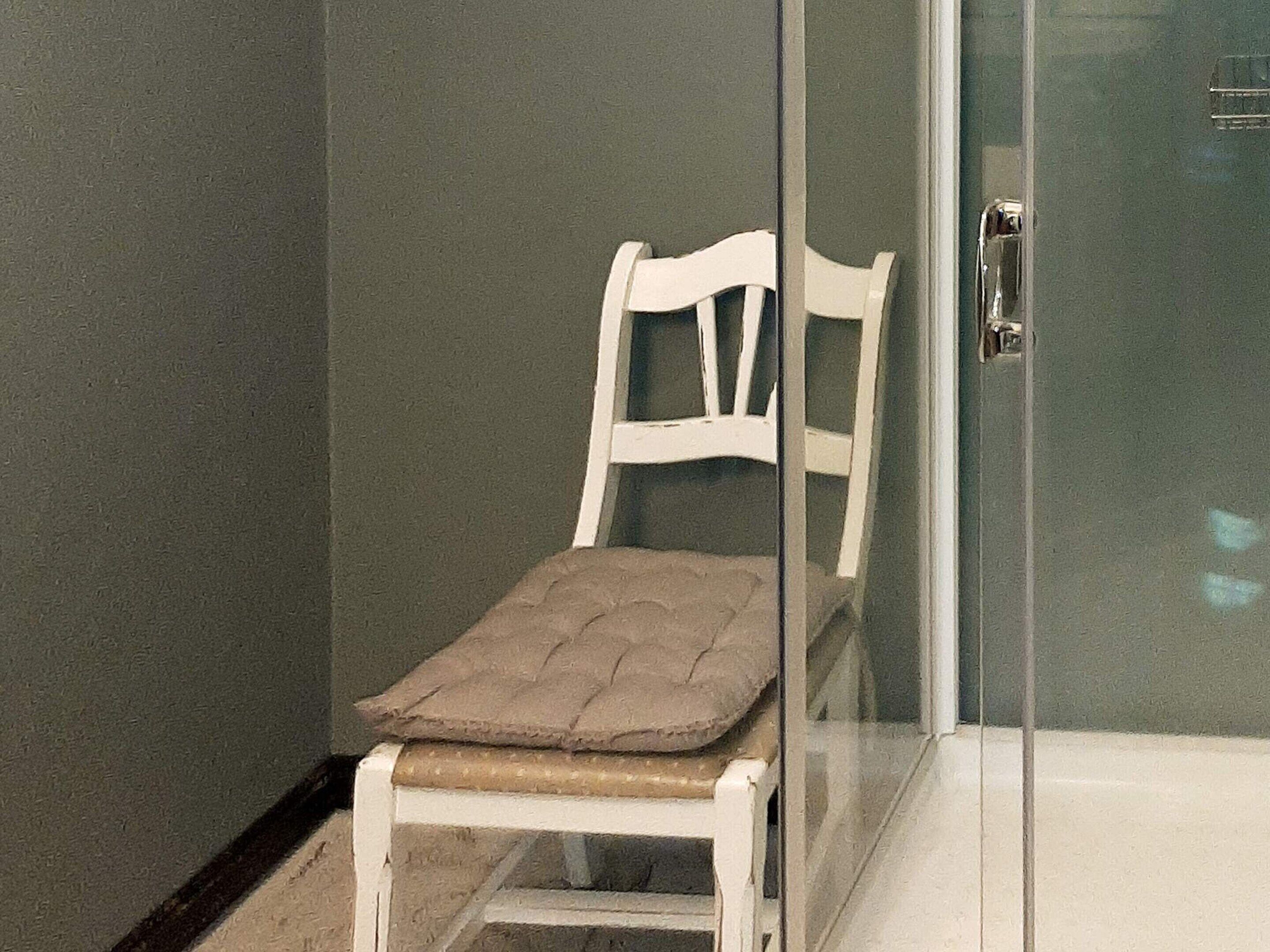 A white chair with a cushioned seat and backrest in a corner of a room with a glass partition.
